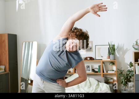 Man Doing Morning Stretching in Bedroom Near Mirror Stock Photo