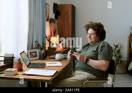Smiling Man Checking Smartphone While Sitting at Desk Stock Photo