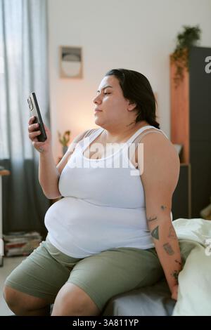 Using Smartphone While Sitting on Bed at Home Stock Photo