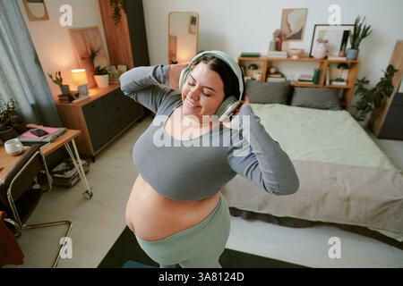 Pregnant Woman Enjoying Music in Cozy Bedroom Stock Photo