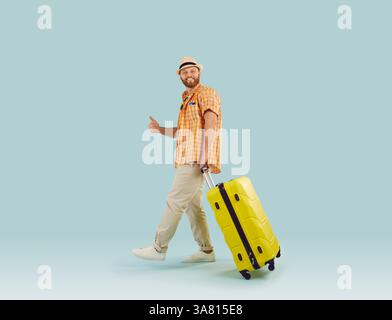 Funny young man in beach hat with suitcase is going on summer holiday on blue background. Stock Photo