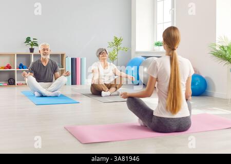 Calm senior people meditating in lotus position, peaceful old practice yoga at club with trainer Stock Photo