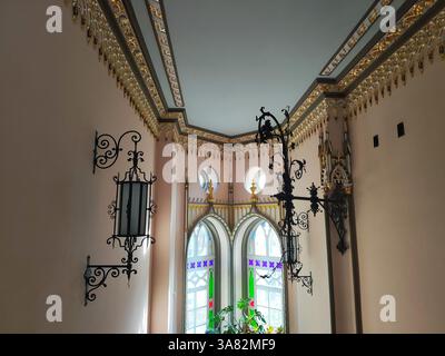 Forged wall lamps in an antique room with patterns on the ceiling and multi-colored windows Stock Photo