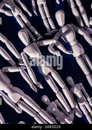 Small wooden artist’s mannequins painted white, posed against a black background. Stock Photo