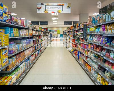 Looking down a supermarket aisle in Waitrose, with cereals, jams, and marmalades on the left, and healthier snacks, crisp multipacks, Free From produc Stock Photo
