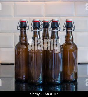 Five brown glass swing-top bottles filled with home-brewed liquid, neatly lined up on a kitchen counter Stock Photo