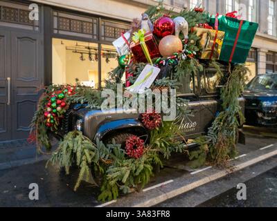 Festively decorated Land Rover Defender 90 adorned with Christmas garlands, baubles, and metallic gift boxes with bows, parked on Savile Row, bringing Stock Photo