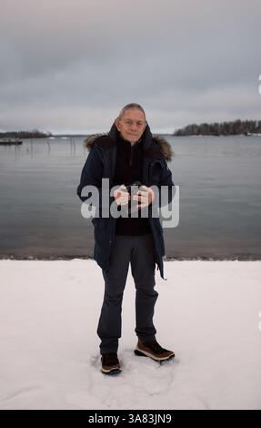 pensioner standing holding his camera by the sea in Sweden Stock Photo