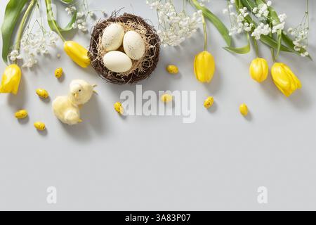 Easter frame with pastel chocolate eggs, tulip flowers, gypsophila and chick on light gray background. View from above. Flat lay. Happy Easter greetin Stock Photo
