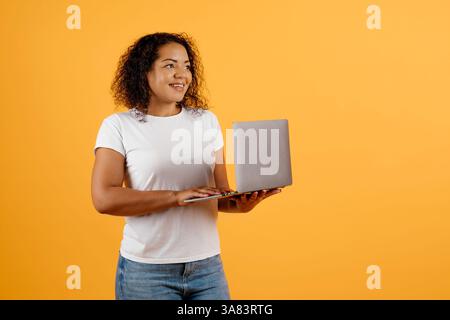 Smiling young African American woman holding laptop and looking aside Stock Photo