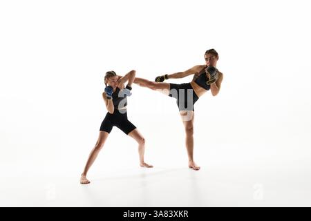 Dynamic image of two competitive and strong women in sportswear and boxing gloves, practicing Thai boxing against white studio background Stock Photo