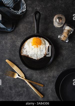 Top view fried egg in pan with plates cutlery on black background. Stock Photo