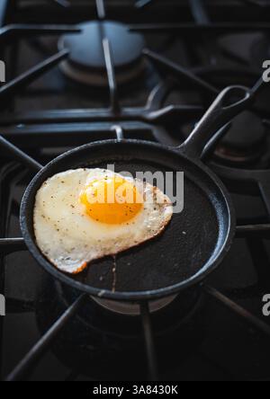 Close up of fried egg cooking in black frying pan on stove. Stock Photo