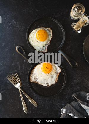 Top view fried eggs in pans with plate forks on black background. Stock Photo