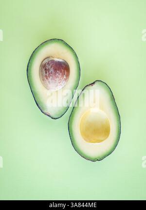 Top view of single avocado cut in half on solid green background. Stock Photo