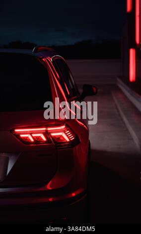 Tail light of modern car in night city. Close-up image of right glowing LED tail light, red neon lines in the background. Stock Photo