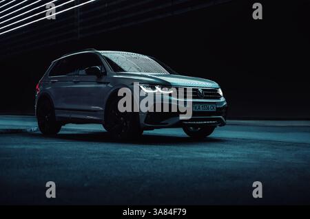 Volkswagen Tiguan on dark city street at night. Front three quarter view of modern SUV at night, glowing LED lines above in the background. Stock Photo