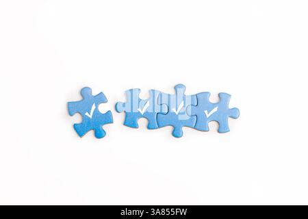 Four blue puzzle pieces with white checkmarks are arranged in a row on white background. represents  completion or agreement, problem-solving Stock Photo