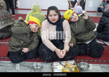 A mother and her twin sons have lunch in a Sikh langar where anyone can get a free vegetarian meal. In a temple in Queens, New York. Stock Photo