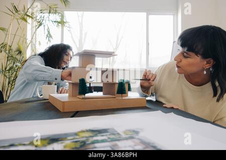 Two project managers engaged in a creative meeting, examine a detailed architectural model. Their discussion suggests teamwork, innovation, and design. Stock Photo