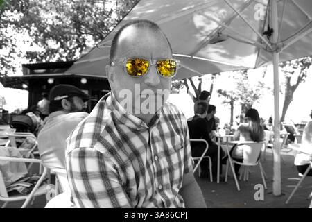 black & white photo of cool middle aged man in check shirt wearing orange reflective sunglasses - spot colour Stock Photo