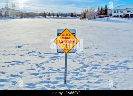 Sign warning of thin ice on a frozen lake in Linden Ridge, Winnipeg, Manitoba, Canada Stock Photo