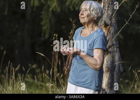 Elderly woman praying with prayer beads in a garden, France Stock Photo