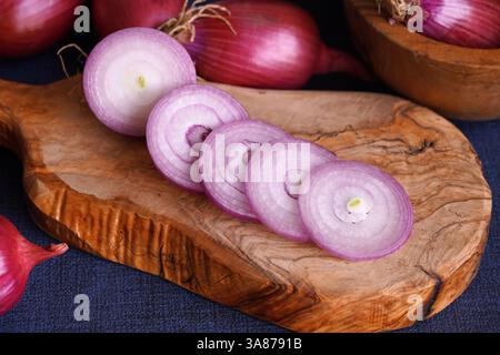 Close up of sliced Tropea red onion on a wooden cutting board and whole red onions in the background. Stock Photo