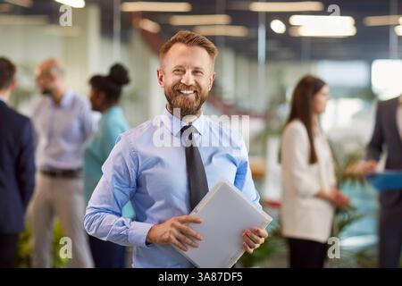 Happy bearded young business man looking at camera and smiling in office. Stock Photo