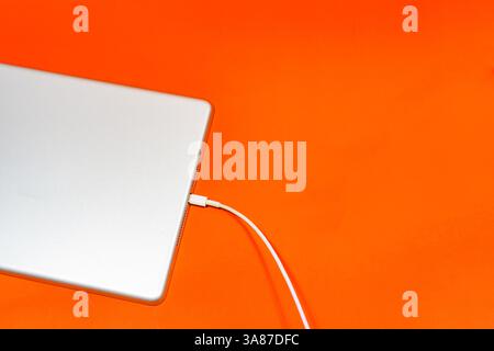Modern device with connected USB cable on orange table Stock Photo