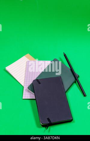 Different types of colored notebooks with a black pen on a green surface Stock Photo
