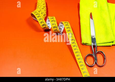 Measuring tape and sewing scissors with a yellow cloth on an orange table. Stock Photo