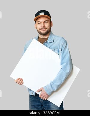 Cutout young adult man in denim joker and snapback holding blank white canvas. Stock Photo