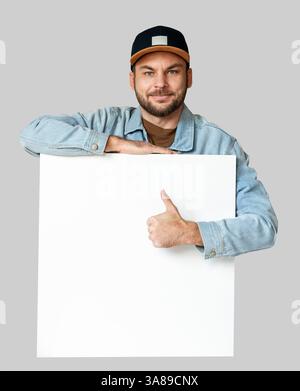 Man wearing casual outfit leaning on blank white board  giving thumbs-up. Stock Photo