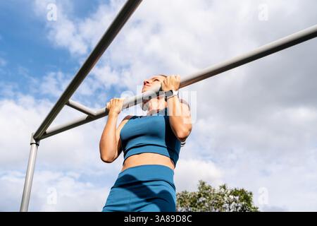 Fit woman doing outdoor workout in fitness park. Female athlete using pull-up bar Stock Photo