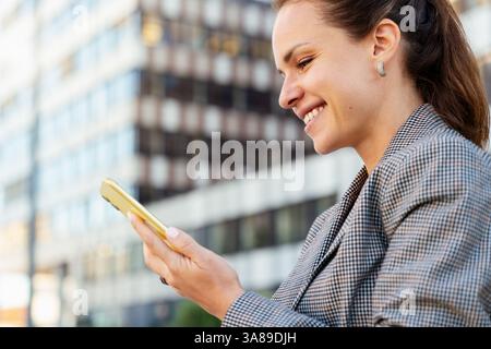 Side view portrait of smiling businesswoman reading message on smartphone Stock Photo