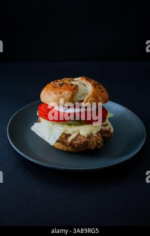 Beef burger with cucumber, tomato, and lettuce on a black plate, featuring a dark food aesthetic and a moody background, captured in vertical format Stock Photo