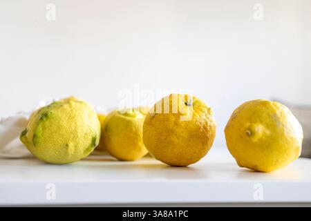 Fresh yellow lemons set on a white table inside, with a white cloth bag behind them. Stock Photo