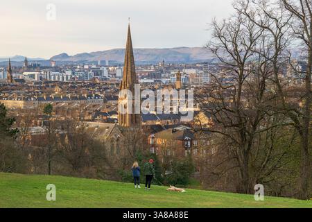 Young couple walking their dog in Queens Park, Looking north across the city centre of Glasgow, Scotland towards the Campsie Hills, Govanhill, Glasgow Stock Photo