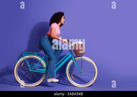 Young woman riding a bicycle against a vibrant purple background, showcasing a stylish and leisurely lifestyle Stock Photo