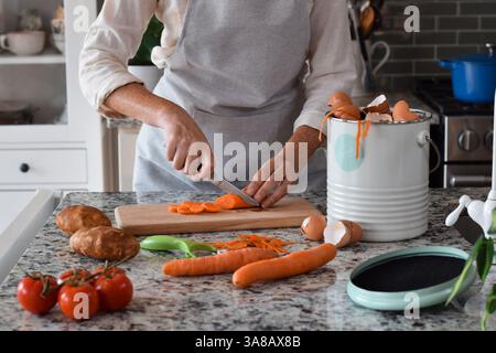 Woman cutting carrots in kitchen and using composter for scraps Stock Photo