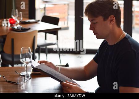 Young man sitting at restaurant table reading menu Stock Photo