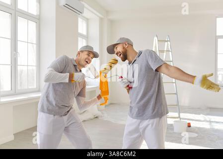 Two cheerful painters foolishing around while having fun, holding paint rollers like microphone Stock Photo