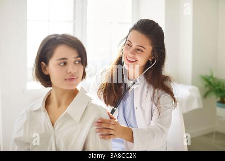 Smiling doctor using stethoscope to check lung health of relaxed woman during medical examination. Stock Photo