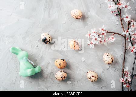 Quail eggs, cherry blossoms and green Easter bunny on gray background. Top view, flat lay. Stock Photo