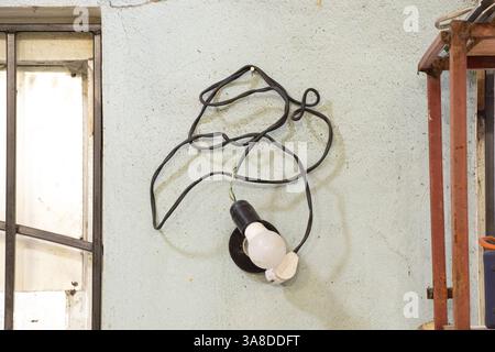 A light bulb in a socket and a black cable hanging on the wall near a socket, lighting in a workshop Stock Photo