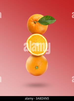 Fresh juicy oranges with green leaf falling on pink gradient background Stock Photo