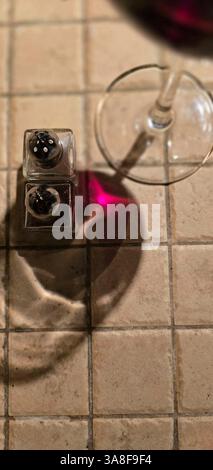 a wine glass projected in the sun on a tiled table with pepper and salt pot Stock Photo