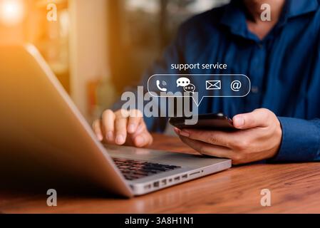 Customer support concept. Man using smartphone and laptop with virtual chat icons for email, phone, and AI chatbot assistance in business communicatio Stock Photo