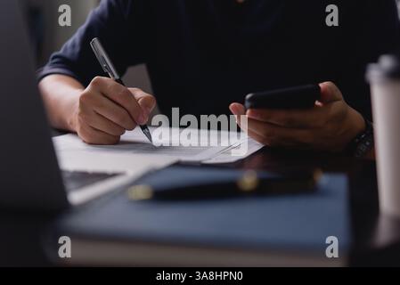 man writing content or a script on a notepad with a pen while holding a phone, highlighting multitasking in work, journalism, or education using a not Stock Photo
